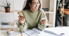 A woman smiles as she holds her phone and a credit card. 