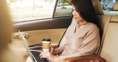 Woman using laptop computer in car while holding a to-go coffee cup