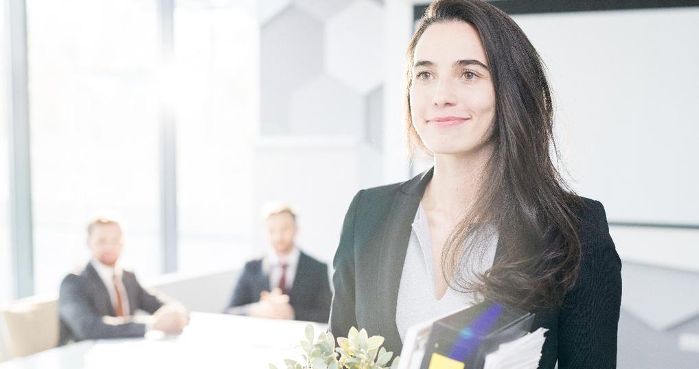  smiling young businesswoman holding box of personal belongings leaving office 