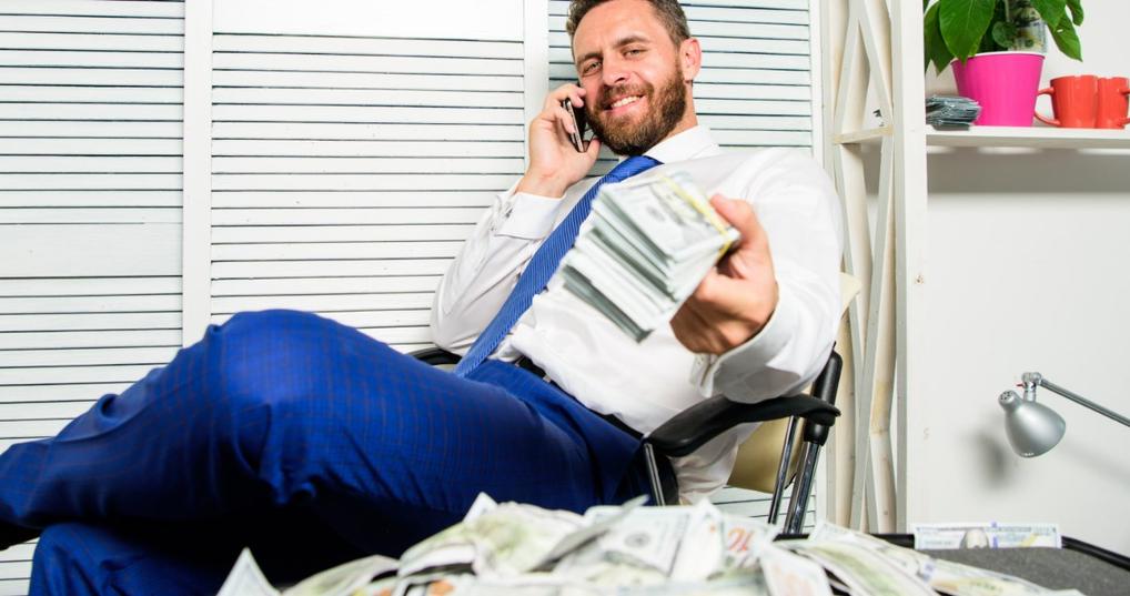 man holding dollars bills while talking on a cellphone