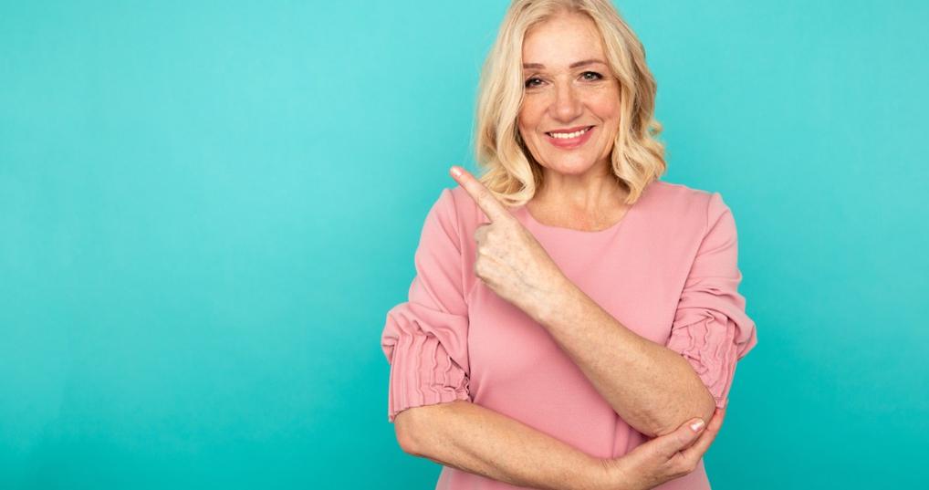 happy woman in short hair raising finger at pink backdrop