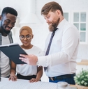 A Black couple looks at a tablet with a white male real estate agent
