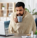 man in blanket with laptop drinking hot tea