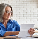 senior lady sitting at table with laptop calculator and cup reviewing taxes at home