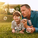 father and son leaning on lawn outdoors playing together while blowing bubbles