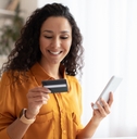 Smiling woman looking at credit card and holding phone