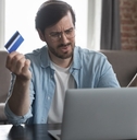 man annoyed at laptop while holding card in hand 