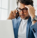 business man holding head in stress while using laptop and talking on smartphone at office
