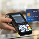 A credit card is held up to a handheld credit card reader. This appears to be at a store checkout.