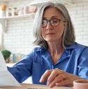 senior mature business woman holding paper bill using calculator managing account finance while sitting at home kitchen table