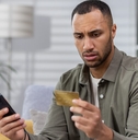 worried man holding card with smartphone