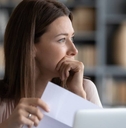 Stressed young woman holding paper document, bank debt notification, looking away.