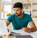 Man holding a credit card and looking at a laptop