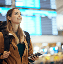 A woman wears a backpack and holds her phone in the middle of an airport.