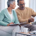 A man and woman look over insurance papers together on a couch.