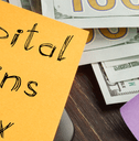 Capital gains tax written on a post-it note next to money