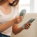 A woman counts a stack of cash on her couch.