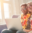 A man and woman wear leis and use a laptop to book their tickets.