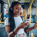 A woman wears headphone and smiles while using her smartphone on a bus.