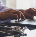 male doctor typing on laptop with medical stethoscope on the desk