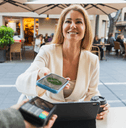 A woman smiles while using her phone to make a payment.