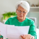 Older woman with white hair looking at paperwork worried
