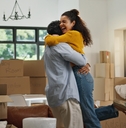 Young couple hugging and celebrating with boxes stacked around them in new house