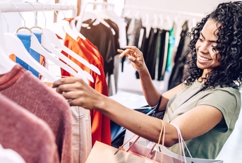 Happy woman exploring rack with hangers in clothes store