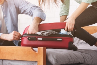 couple stuffing suitcase to avoid baggage fees