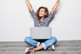 woman with laptop arms in air celebrating