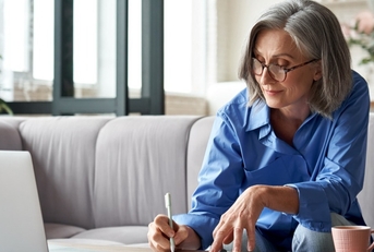 Woman in her fifties at computer writing down notes 