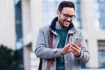 A smiling man outside wearing a coat and looking at his phone.
