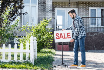Man putting for sale sign in front of house