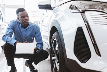 serious auto salesman sitting near new car