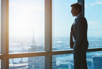 mature businessman looking through large windows at city below