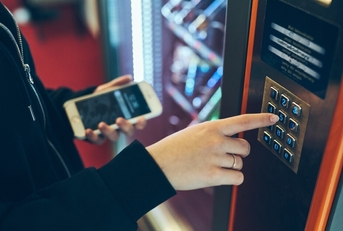A close-up of a woman's hand as she presses buttons on a vending machine to purchase a snack.