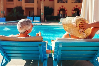 senior couple relaxing by swimming pool lying on chaise-longues