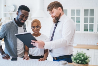 A Black couple looks at a tablet with a white male real estate agent