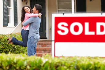 hispanic couple outside home with sold sign