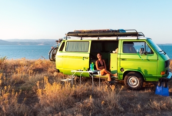 Young attractive female sitting in old timer camper van on a hill 