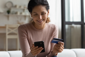 Smiling woman looking at her phone and holding a credit card