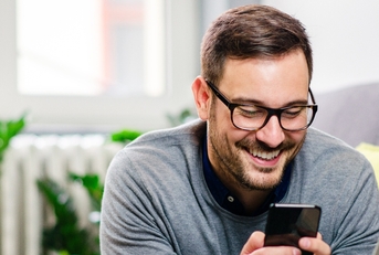 Young man with glasses smiling while using phone