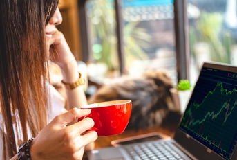 adult woman holding a coffee cup while looking at a stock chart on her laptop