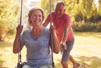 retired couple having fun with man pushing woman on garden swing