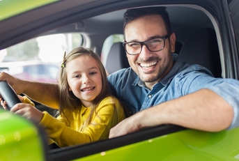 father and daughter smiling behind a driving wheel