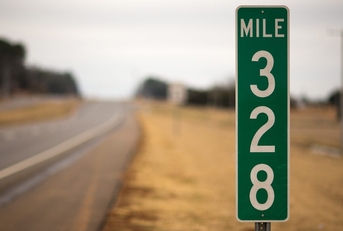 A green mile marker on an empty road.
