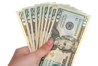 A hand holds several 20-dollar bills arranged in a fan 