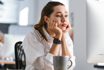 bored young woman dressed in shirt sitting at her workplace