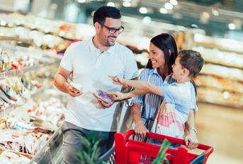 family with child and shopping cart buying food at grocery store