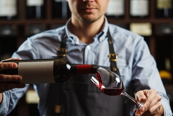 male sommelier pouring red wine into long-stemmed wine glasses